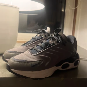 Grå sneakers från Nike - Snygga grå sneakers från Nike med en modern design och svarta detaljer. Skorna har en bekväm sula med synliga luftkuddar och snörning för perfekt passform. Perfekta för både vardag i storlek 38 