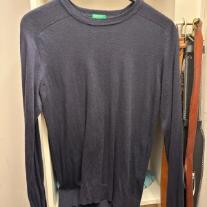 Mörkblå tröja från Benetton - Säljer en stilren mörkblå tröja från Benetton. Tröjan har en klassisk rund hals och långa ärmar, perfekt för kyligare dagar. Den är tillverkad i ett mjukt material som ger en bekväm passform. Passar bra till både jeans och chinos.