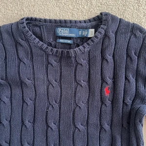 Mörkblå stickad tröja från Ralph Lauren för kvinnor - Säljer en snygg mörkblå stickad tröja från Ralph Lauren för kvinnor med kabelstickat mönster. Tröjan har en rund halsringning och det ikoniska röda logotypbroderiet på bröstet. Tröjan är i storlek xs och jag säljer pga att den har blivit för liten. Ordinariepris är 2395kr❤️❤️