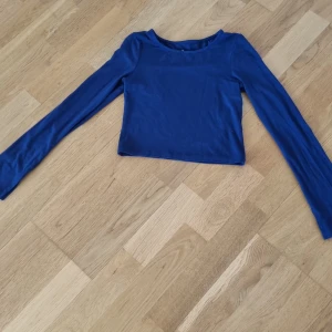 Blå långärmad croppad topp - Säljer en snygg blå långärmad topp från märket C. Toppen är croppad och har en enkel design som passar perfekt till olika outfits. Materialet känns mjukt och bekvämt mot huden.