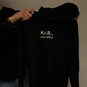 Svart hoodie från Karl Lagerfeld - Snygg svart hoodie från Karl Lagerfeld med tryck på både fram- och baksidan. Perfekt för en stilren och modern look.
