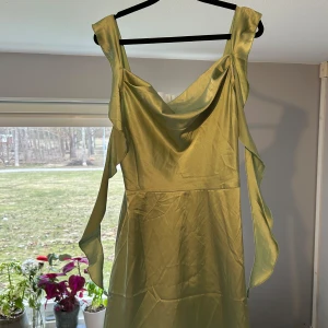 Grön klänning i satin med volangdetaljer - Snygg grön klänning med volangdetaljer och breda axelband. Klänningen har en elegant drapering framtill och är perfekt för en somrig look. Materialet ger en fin glans och faller vackert. Köpt på Cider för 400 kr.