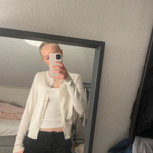 Vit kofta med knappar - Säljer en stilren vit kofta med knappar framtill. Perfekt för lager-på-lager och passar till många olika outfits. Koftan har långa ärmar och en klassisk design.