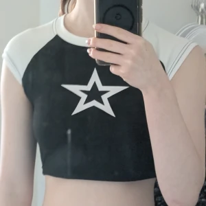 Svart och vit croppad topp med stjärna - Snygg svart och vit croppad topp med en stor vit stjärna på bröstet. Toppen har korta ärmar. Perfekt för en trendig look! Är xxs men passar xs