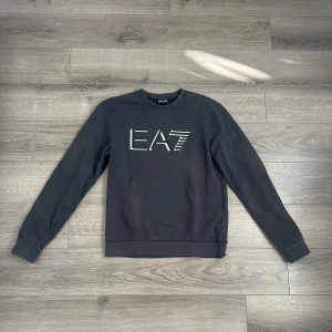 Svart sweatshirt från Emporio Armani - Säljer en stilren svart sweatshirt från Emporio Armani med EA7-logga på bröstet. Nypris 800kr, mitt pris, 200kr