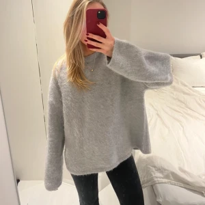 Grå stickad tröja - Mysig grå stickad tröja med en avslappnad passform. Perfekt för kyliga dagar med sina långa ärmar och mjuka material. Enkelt att matcha med olika outfits. (Moahir och alpacka)