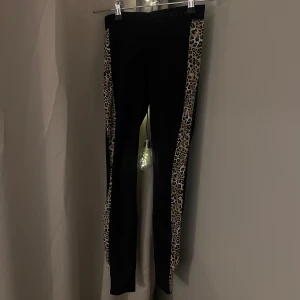 Svarta leggings med leopardmönster från Guess - Snygga svarta leggings från Guess med leopardmönstrade paneler längs sidorna. Elastisk midja för bekväm passform.