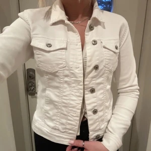 Vit jeansjacka med knappar - Snygg vit jeansjacka från only med knappar framtill och två bröstfickor i storlek 36. Användes förra våren och efter det bara legat i garderoben så den är i väldigt fint skick! Lätt att tvätta i tvättmaskinen om det skulle behövas😊