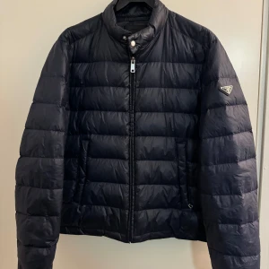 Prada Dunjacka Marinblå - Prada Dunjacka storlek 50 passar M. Skick 8/10. Tror den är fråk 2014 kollektionen. Hör av dig för mer info och bilder. Inga skador eller defekter 