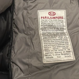 Svart dunjacka från Parajumpers - Säljer en svart dunjacka från Parajumpers med huva och dragkedja. Jackan har ett broderat märke på ärmen och är perfekt för kalla dagar. Den är designad för att klara extrema förhållanden och har en stilren look. Jackan passar längden 140-160 cm slim