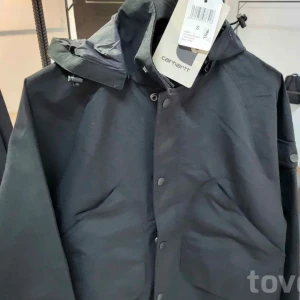 Carhartt WIP CLARTON JACKET - Säljer en stilren svart  från Carhartt. Jackan har en praktisk huva och knäppning framtill. Perfekt för blåsiga dagar och har en klassisk design som passar till det mesta.