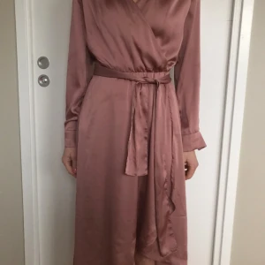 Rosa satin klänning Stl 34 Ny - Klänning i en vacker rosa nyans. Polyestersatin. Klänningen har långa ärmar och knyt i midjan. H&M party collection. Stl 34, passar en small. Ny. Nypris 499:-