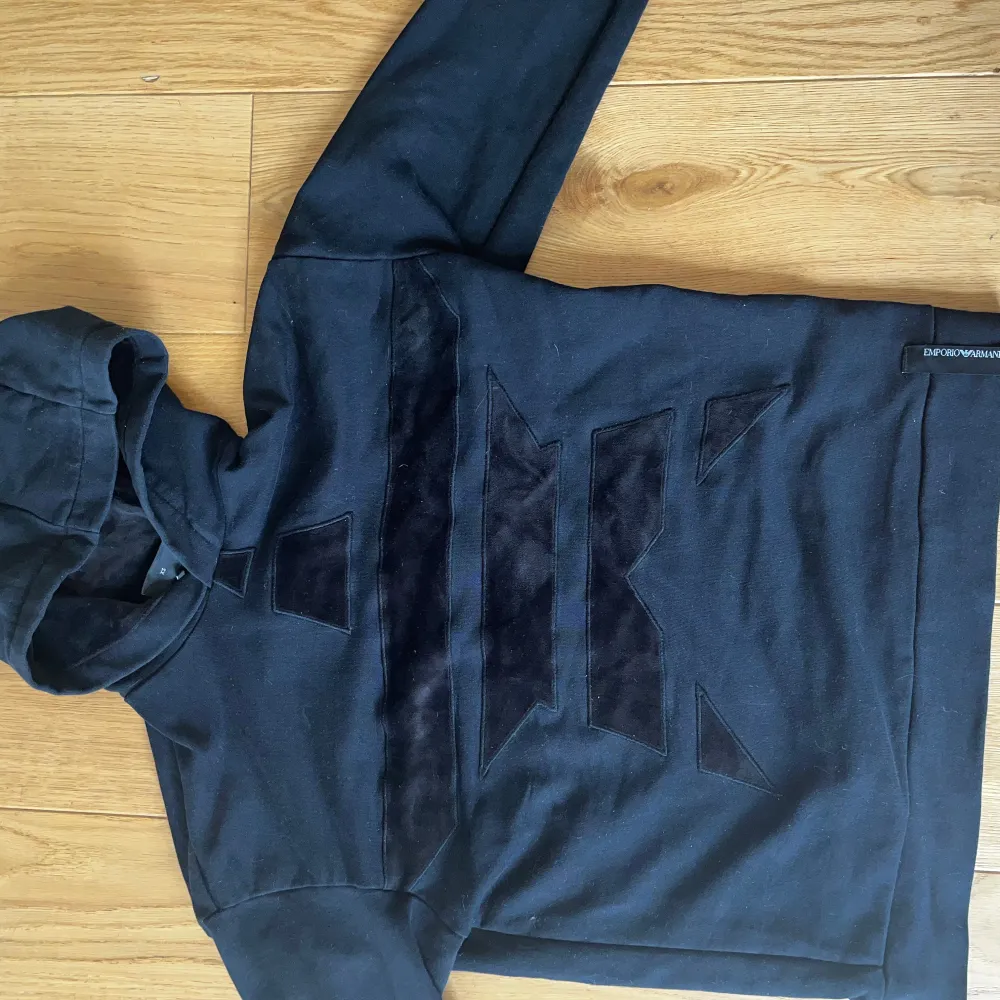 Snygg svart hoodie från Emporio Armani med ett unikt geometriskt mönster på framsidan. Tröjan har en klassisk huva och långa ärmar, perfekt för en stilren look. Den är tillverkad i ett mjukt material som ger en bekväm passform.. Hupparit & Collegepaidat.