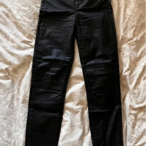 Svarta högmidjade jeans från Karve - Svarta högmidjade jeans från Karve. De har en tight passform och är tillverkade i en blandning av bomull och polyester med en cool coated finish. 