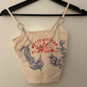 Beige ribbad linnetopp från Cape Clique - Snygg beige ribbad linnetopp från Cape Clique med coolt draktryck i blått och rött. Toppen har smala axelband och en kedjedetalj framtill som ger en edgy look. Perfekt för att sticka ut i mängden!