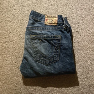 True Religion lågmidjade jeans - Säljer ett par snygga blå jeans från True Religion med klassisk logga på bakfickan och kontrastsömmar. Lågmidjade!! Kan tänka mig att sänka priset vid smidig affär!! Skriv för mått.        Köpte de från plick men de passade inte mig💗