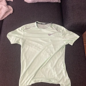 Nike Dri-Fit ljusgrön t-shirt - Nike Dri-Fit t-shirt i ljusgrönt med klassisk Swoosh-logga på bröstet. Tillverkad i ett lätt och ventilerande syntetmaterial som är perfekt för träning. T-shirten har rund hals och korta ärmar, samt diskreta sömdetaljer vid axlarna.