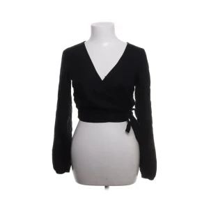 Svart topp från Hollister - Svart omlottopp från Hollister med lång ärm och v-ringad hals. Toppen har en snygg knytning i sidan och är croppad