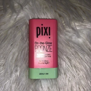 Pixi On-the-Glow Bronze stick - Säljer en Pixi On-the-Glow Bronze stick i en snygg rosa och mintgrön förpackning. Perfekt för att ge ansiktet en solkysst glow med enkel applicering direkt från stiftet. Innehåller 19g och är smidig att ta med i väskan.