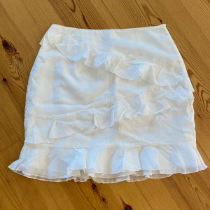 Vit kortkjol med volanger - Superfin vit kortkjol med flera volangdetaljer från Nelly. 