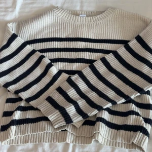 Randig stickad tröja i beige och svart - Säljer en ribbstickad tröja med breda svarta ränder på beige botten. Tröjan har rund hals och långa ärmar, perfekt för dig som gillar klassisk och chill stil. Materialet är mjukt och stickat, vilket gör den skön att bära under kyliga dagar. Likadan fast svart vit randig.