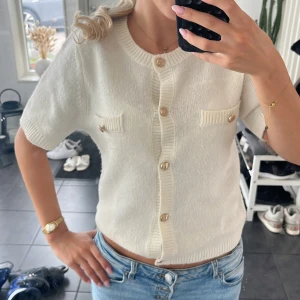 Vit stickad kortärmad blus med knappar - Superfin vit stickad blus med korta ärmar och snygga guldfärgade knappar framtill. Knappt använd. Storlek 170