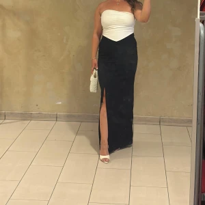 Svart och vit axelbandslös långklänning - Säljer en stilren långklänning med axelbandslös vit överdel och svart kjol med slits framtil. Klänningen har en snygg v-ringad skärning vid midjan och är perfekt för dig som vill ha en elegant look. Passar dig som gillar minimalistisk stil och att sticka ut. Köpt från asos. Passar även en 42. 