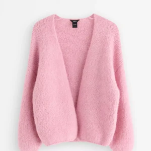 Rosa fluffig kofta från Lindex - Mysig och fluffig rosa kofta från Lindex med loose passform och långärmade ärmar. Koftan har en öppen front utan knappar och är stickad i ett mjukt material som känns skönt mot huden. Perfekt för att addera lite färg till din outfit.