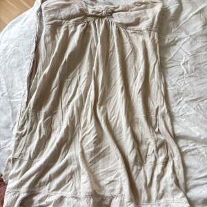 Beige kort klänning Abercrombie & Fitch - Snygg beige kort klänning från Abercrombie & Fitch med axelbandslös design och smock upptill. Tillverkad i mjuk bomull, med diskret broderad logga på sidan. Perfekt för varma dagar och enkel att styla med accessoarer.