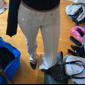 Beige jeans H&M  - Snygga beige bootcut-byxor från H&M Divided med fickor framtill och knappdetaljer. Byxorna har låg midja och är gjorda i mjuk bomull med lite stretch för skön passform. Perfekt till en cool och avslappnad stil.
