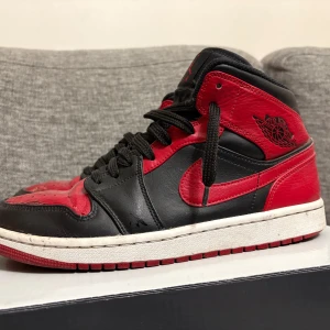 Nike Air Jordan 1  - Säljer ett par ikoniska Nike Air Jordan 1 sneakers i svart och rött skinn. Klassisk high-top siluett med rund tå, snörning och vit/röd yttersula. Snyggt Jordan Wings-logo på sidan och Jumpman på plösen. Perfekt för dig som vill sticka ut med en tidlös streetwear-look.