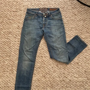 Blå jeans från Jacob Cohën - Snygga blå jeans från Jacob Cohën med klassisk femficksdesign och orangea kontrastsömmar. Märkets logga syns på bakfickan och ett brunt patch med metalltext bak i midjan. Jeansen har rak passform och är tillverkade i mjukt denimtyg.