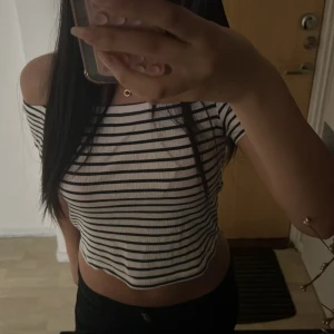 Randig offshoulder croppad topp - Säljer en vit och svart randig croppad topp med offshoulder-design. Toppen har en tight passform och är tillverkad i mjuk bomull. Perfekt för dig som gillar en enkel men snygg stil med lite edge.