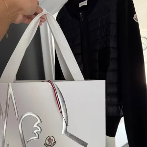 Svart cardigan jacka från Moncler - Säljer min cardigan från Moncler som jag köpte i Paris, endast använd 5 gånger så den är som ny, men kommer inte till användning❣️nypris för jackan just nu är 9,5 tusen kr. jackan har en quiltad front och ärmar i mjuk ull, Moncler-logga på ärmen, dragkedja framtill och stilren design. Materialmix av dun, polyester och ull gör den både lätt och varm. Perfekt nu inför hösten och kallare tider!! Pris går att diskutera😚den har inga defekter eller fläckar❣️