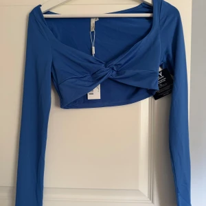 Blå croppad twisttopp från NLY Trend - Snygg blå croppad topp från NLY Trend i storlek XS. Toppen har lång ärm och en cool twistad detalj framtill som ger en unik look. Tillverkad i mjuk polyester med stretch för skön passform. Perfekt att styla med höga jeans eller kjol för en trendig vibe.