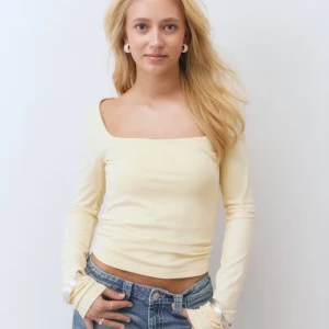 Ljusgul långärmad topp från gina - Säljer en ljusgul långärmad topp från gina med fyrkantig halsringning och slim passform. Toppen är croppad och har mjukt, stretchigt material i bomull. Perfekt att styla med jeans för en chill look.