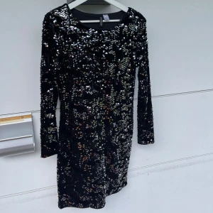 Svart paljettklänning från H&M - Säljer en svart kort klänning från H&M med massor av glittriga paljetter i silver Klänningen har lång ärm och rund halsringning, perfekt för att sticka ut på festen. Materialet är mjukt och stretchigt för skön passform.Storlek är märkt som 42 men enligt mig är det mer M/L Aldrig använd 