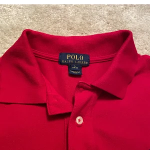 Röd Polo Ralph Lauren pike - Snygg röd piké från Polo Ralph Lauren med klassisk pikékrage och två knappar framtill. Ikoniska broderade loggan i svart på bröstet. Piken är kortärmad och gjord i mjuk bomull, perfekt för en chill och stilren look. Den är också slimfit Skick 9/10 priset ej hugget i sten😇 hör av dig om de är något du undrar över ☺️