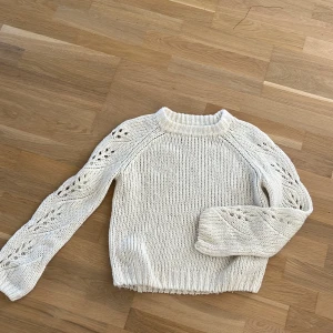 Vit stickad tröja med hålmönster - Säljer en vit stickad tröja från C i storlek 158/164, men den funkar till stolek 34/36. Tröjan har långärmade ärmar med snyggt hålmönster längs hela ärmarna och ribbad kant vid hals, ärmslut och nederkant. Perfekt för dig som gillar en chill och mysig stil.