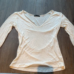 Ribbad beige långärmad tröja från Zara - Säljer en beige ribbad långärmad tröja från Zara i storlek S. Tröjan har en snygg v-ringad hals och är gjord i ett mjukt, stretchigt material som sitter skönt mot kroppen. Perfekt att styla med jeans eller kjol för en clean look.