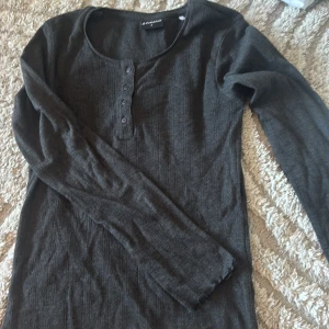 Mörkgrå ribbad långärmad tröja Firefly - Säljer en mörkgrå långärmad tröja från Firefly i storlek S. Tröjan har ribbad struktur, rund halsringning och fyra knappar framtill. Materialet känns mjukt och stretchigt, perfekt för chill dagar. Ärmsluten har en lätt vågig kant för extra stil.