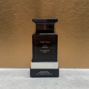 Tom Ford Oud Wood EdP 100ml - Exklusiv parfym från Tom Ford, Oud Wood Eau de Parfum i 100 ml flaska. Flaskan är mörkgrå och svart med en lyxig, fyrkantig design och silverdetaljer. Doften är känd för sina träiga och mystiska noter, perfekt för dig som gillar unika och sofistikerade parfymer.