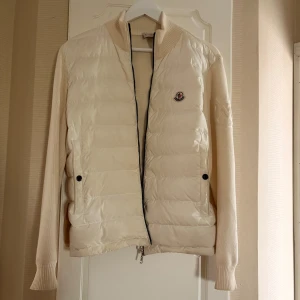 Moncler cardigan  - Snygg beige cardigan från Moncler med stickade ärmar och broderad Moncler-logga på ärmen. Framsidan är quiltad med dunfyllning och har två fickor med knappar samt dragkedja. Pris kan diskuteras🥰