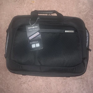 Svart datorväska Samsonite Vectura - Snygg och stilren svart datorväska från Samsonite, modell Vectura. Väskan har flera fack, dragkedjor och ett handtag upptill. Passar för laptop upp till 16 tum. Tillverkad i slitstark polyester med diskret logga på framsidan.(Priset kan diskuteras)