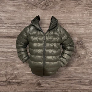 Mörkgrön pufferjacka Peak Performance - Snygg mörkgrön pufferjacka från Peak Performance med huva och dragkedja framtill. Jackan har en quiltad design och är tillverkad i syntetmaterial, perfekt för kalla dagar. Passformen är normal och jackan har långa ärmar. En stilren och funktionell vinterjacka. 