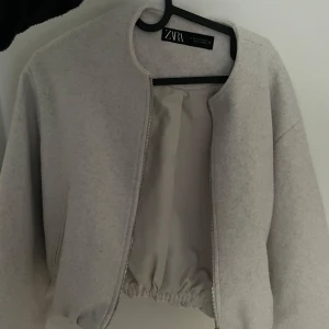 Beige bomberjacka från Zara XS - Snygg beige bomberjacka från Zara i storlek XS. Jackan har en croppad passform med resår i midjan, dragkedja framtill och rund halsringning. Tillverkad i ett mjukt material som känns både stilrent och bekvämt. Perfekt för dig som gillar minimalistisk och clean stil.