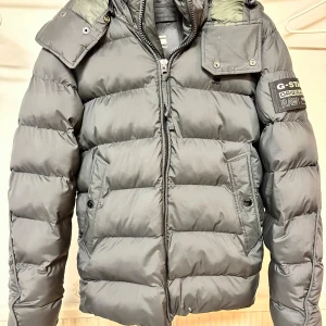 Stilren och varm jacka för tonårskille - Jacka i mycket fint skick, perfekt för en 15-17åring. Har hög krage och huva som skyddar mot vind och kyla. Snygg, bekväm och redo för både skola och fritid