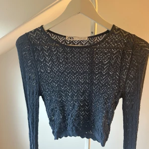 Mörkblå croppad topp från Zara - Snygg mörkblå croppad topp från Zara med lång ärm och transparent stickat mönster. Toppen har en rund halsringning och ett coolt zigzag-mönster som ger en unik vibe. Perfekt att styla med höga jeans eller kjol för en trendig look.