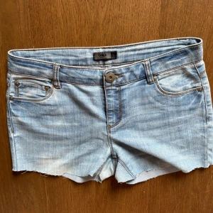 Ljusblå jeansshorts från ONLY - Snygga, lågmidjade, ljusblå jeansshorts från ONLY med klassisk femficksdesign, slitna kanter och kontrastsömmar. Shortsen har knapp och dragkedja framtill samt bälteshällor. Fint skick! Skulle uppskatta att stoleken är ungefär som S.