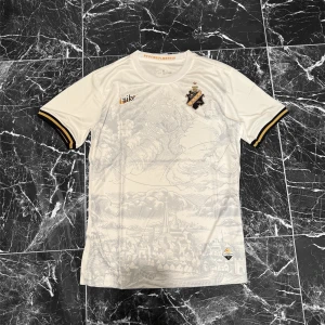 AIK x Nike vit fotbollströja - AIK fotbollströja från Nike i vit polyester med subtilt stadsmotiv över hela framsidan. Svart och guld AIK-emblem på bröstet, samt Nike-logga i guld. Svarta och gula detaljer på ärmsluten ger extra stil. Perfekt för dig som vill representera AIK.